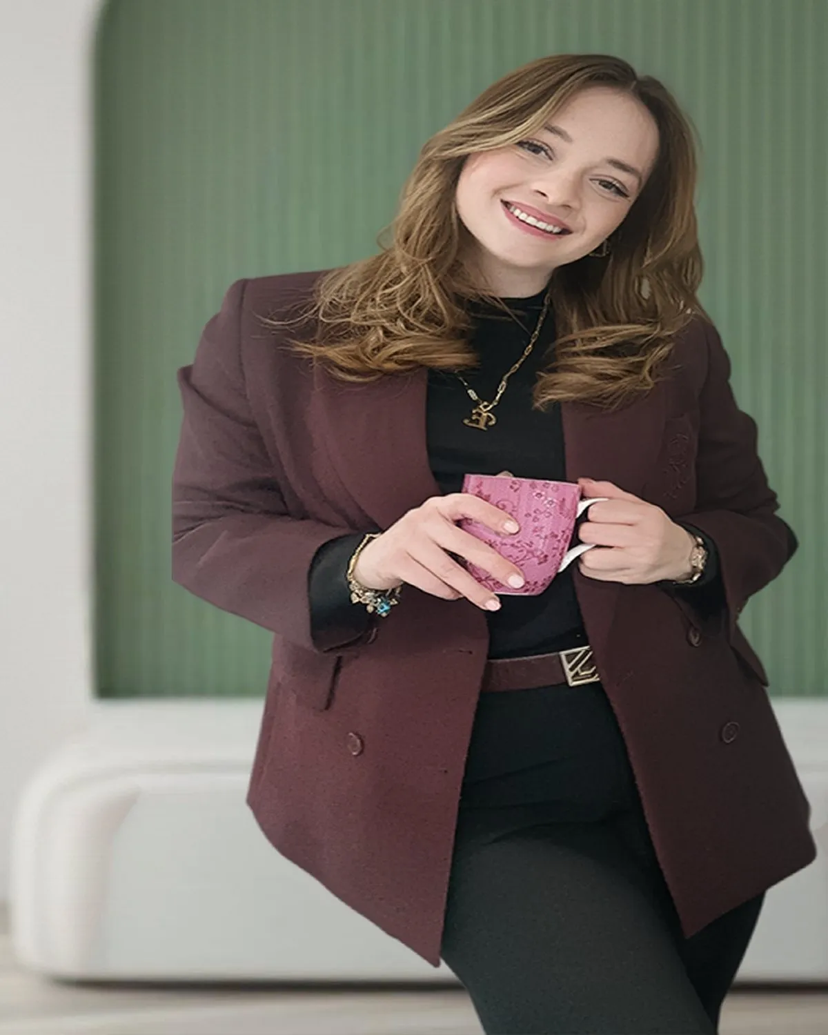 Uzman Klinik Psikolog Elif Zeynep Erbir, yeşil bir duvarın önünde elinde fincanla gülümsüyor